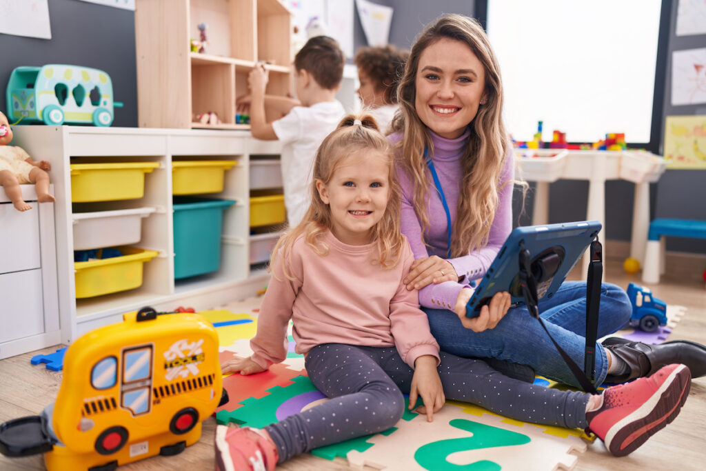 Woman and group of kids having lesson using touchpad at kindergarten
